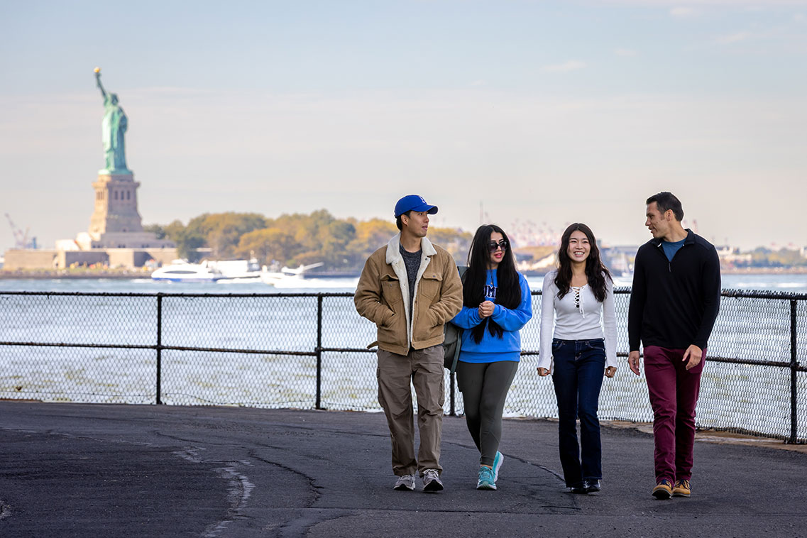 Four Columbia SIPA students walking together along a New York City waterfront path with the Statue of Liberty in the background